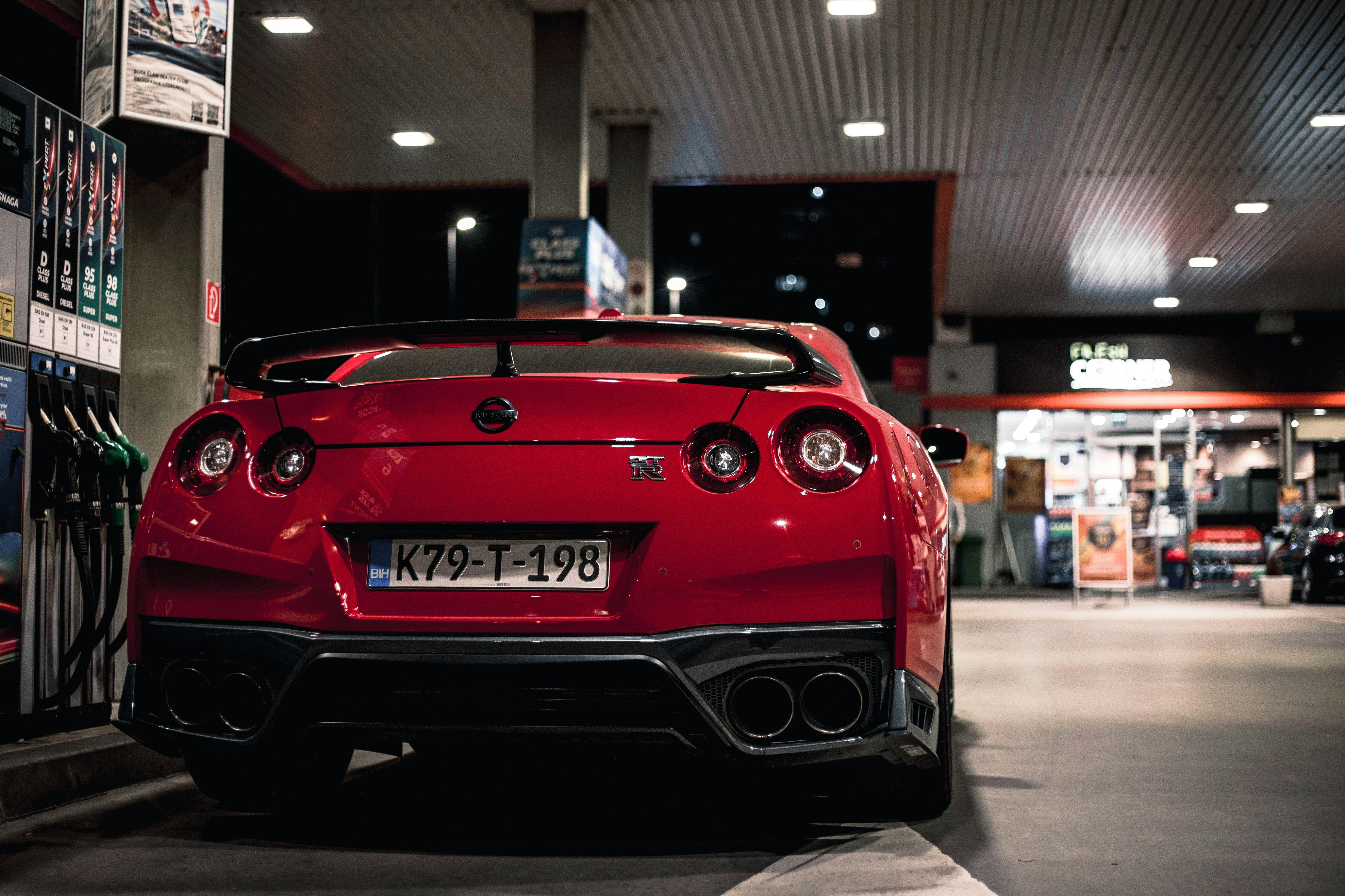 The rear view of a red Nissan GT-R parked at a brightly lit gas station at night, showing its iconic round taillights.