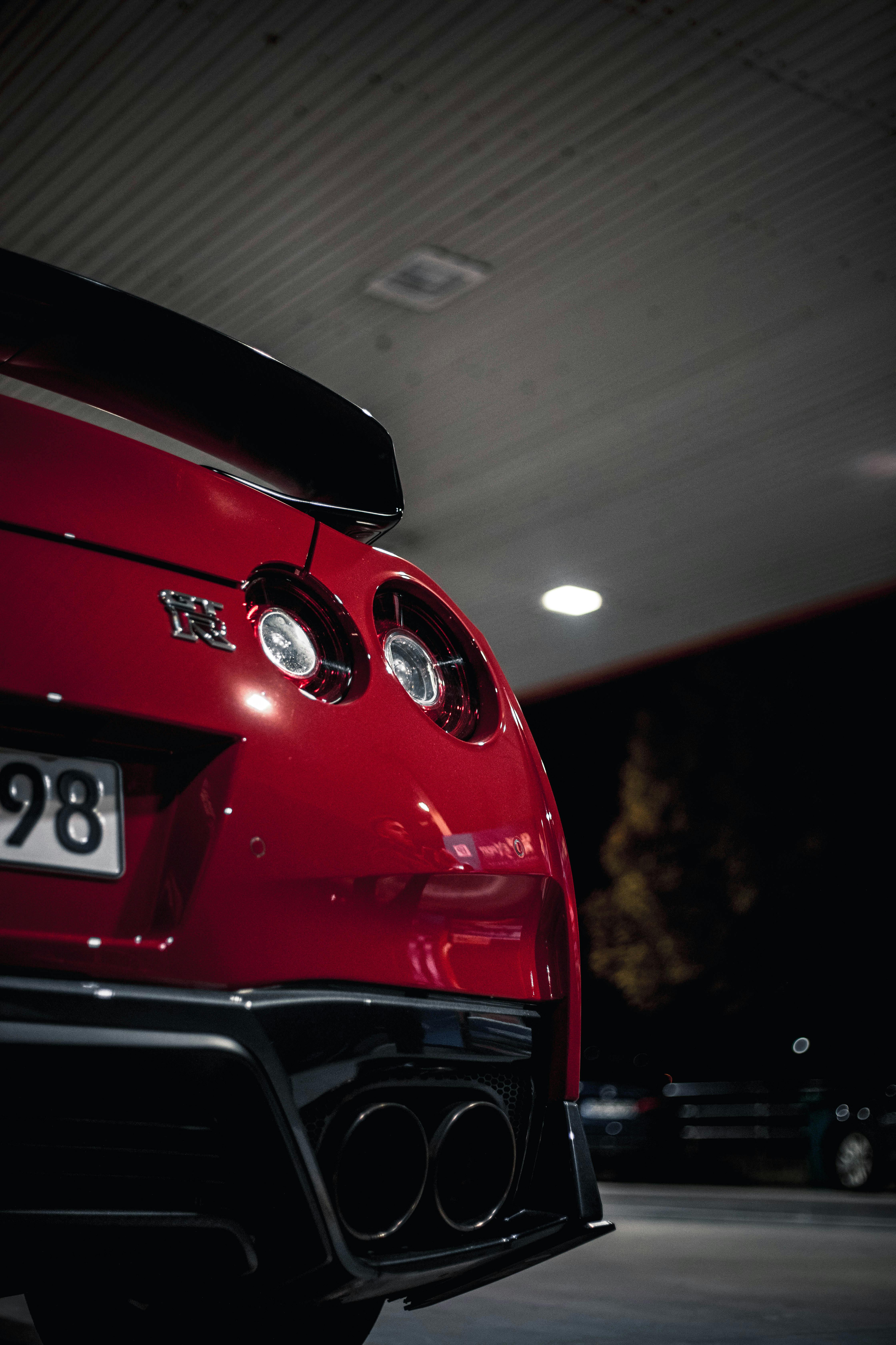 A tight, artistic close-up of the rear quarter panel and signature round taillights of a red sports car under overhead garage lights.
