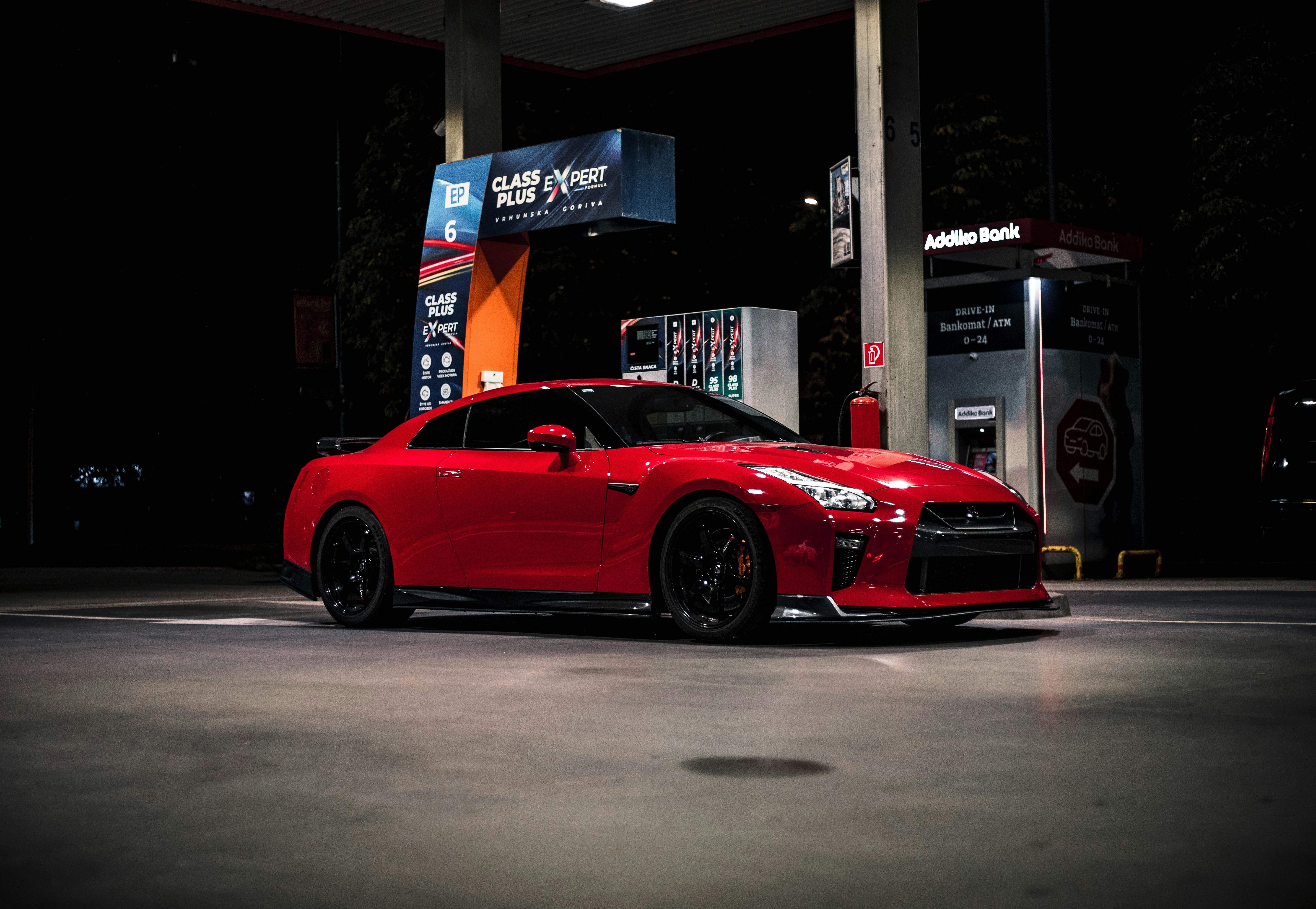 A profile shot of a sleek red Nissan GT-R parked at a gas station under fluorescent lights at night.