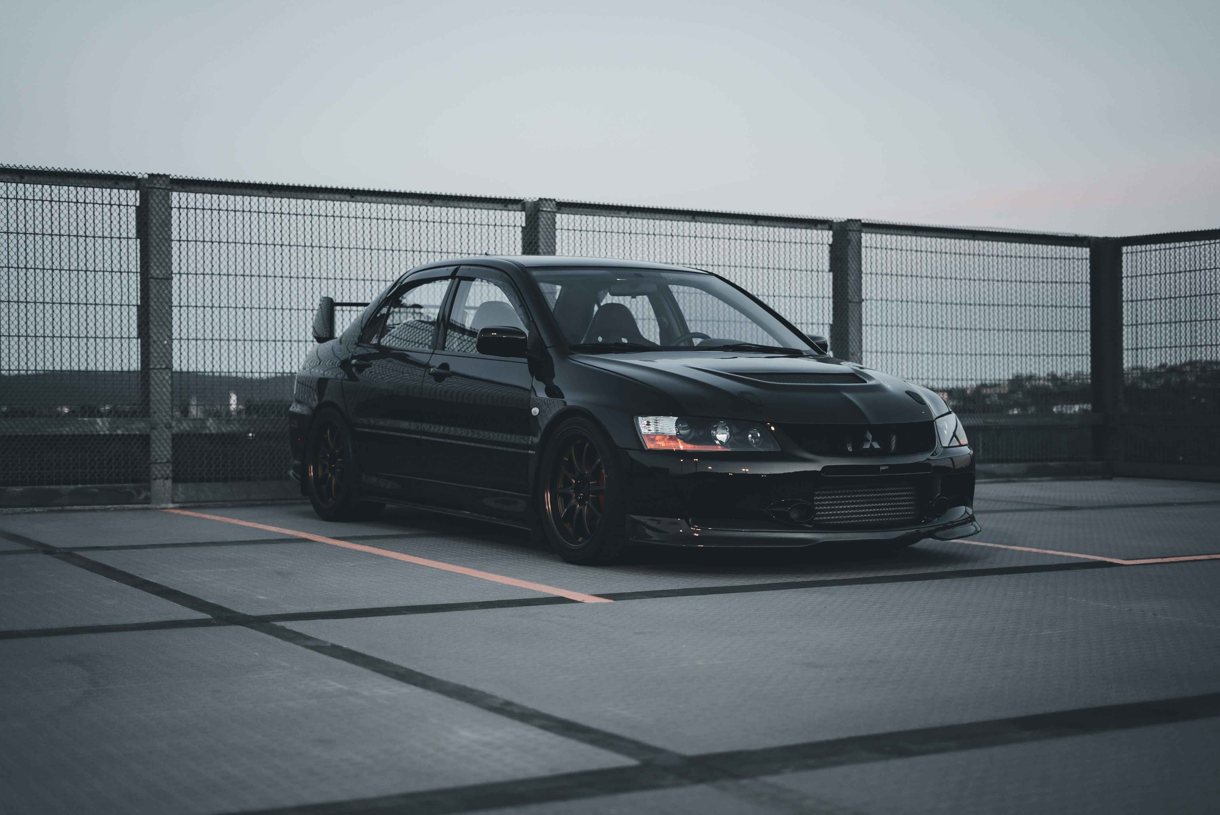 A black Mitsubishi Lancer Evolution parked on an empty rooftop parking lot at dusk, showcasing its high rear wing.