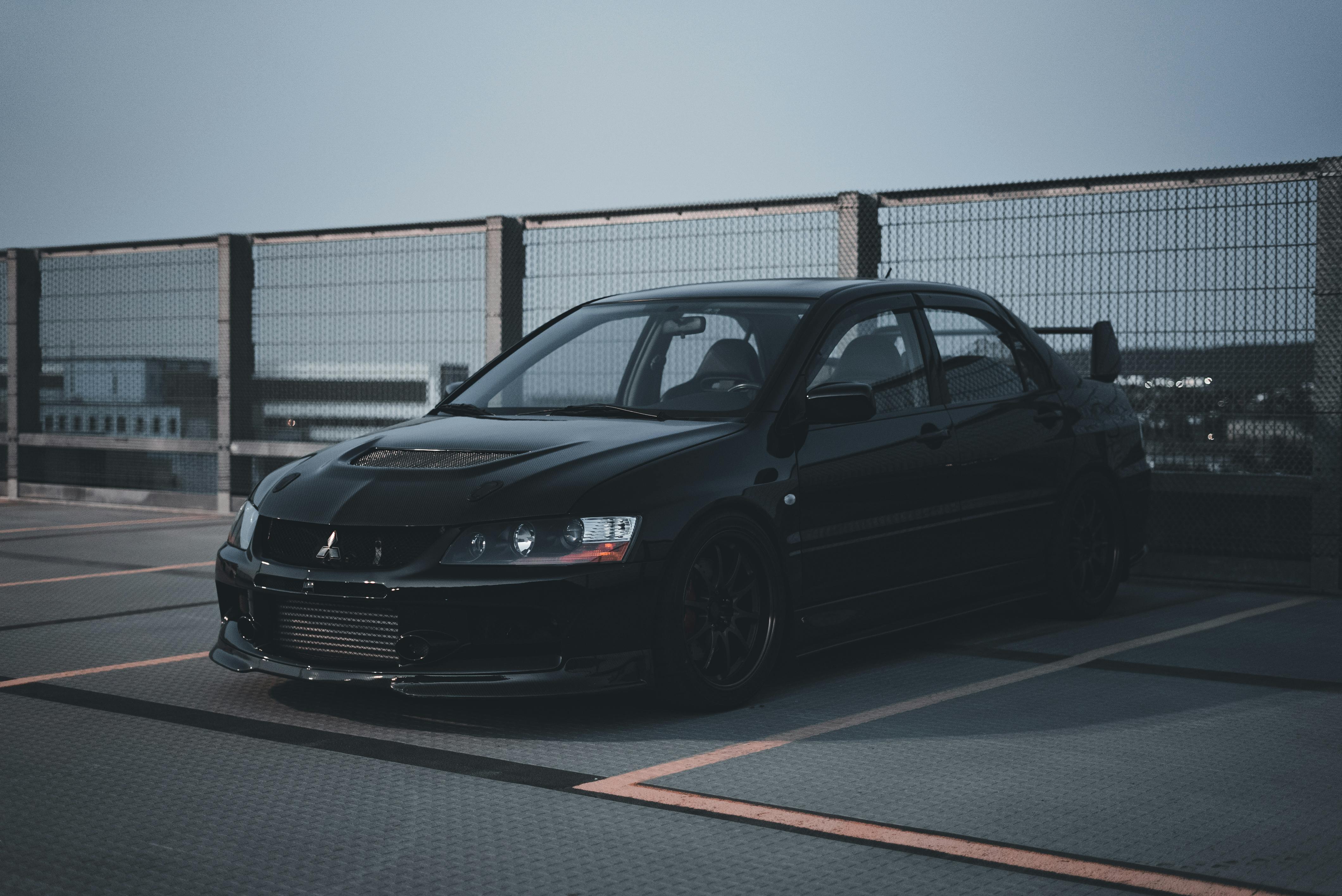 A front-three-quarter view of a black Mitsubishi Lancer Evolution parked in a paved lot under overcast lighting.