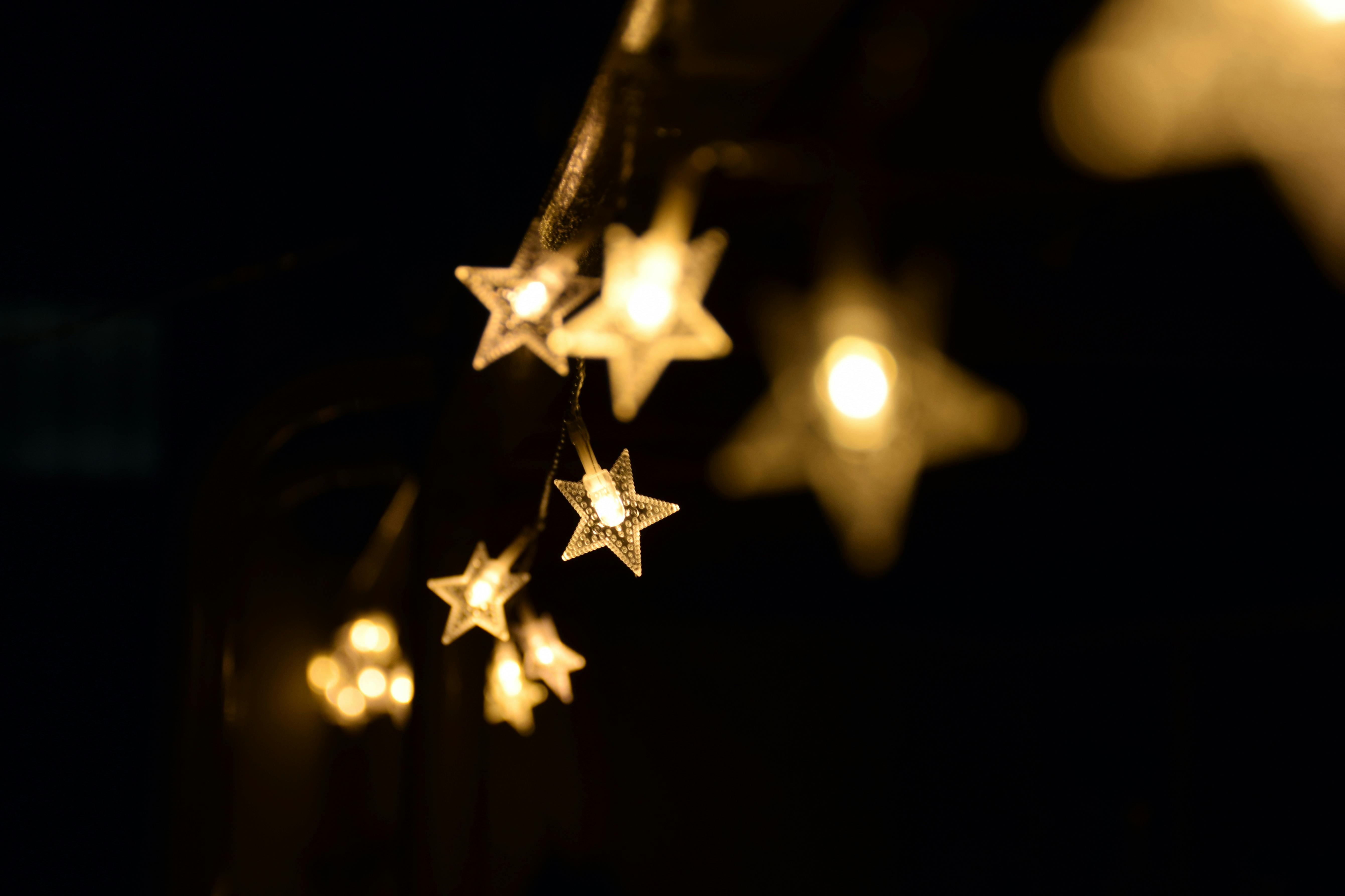 Close up, shallow depth of field shot of warm, star shaped fairy lights glowing against a dark, out of focus background.