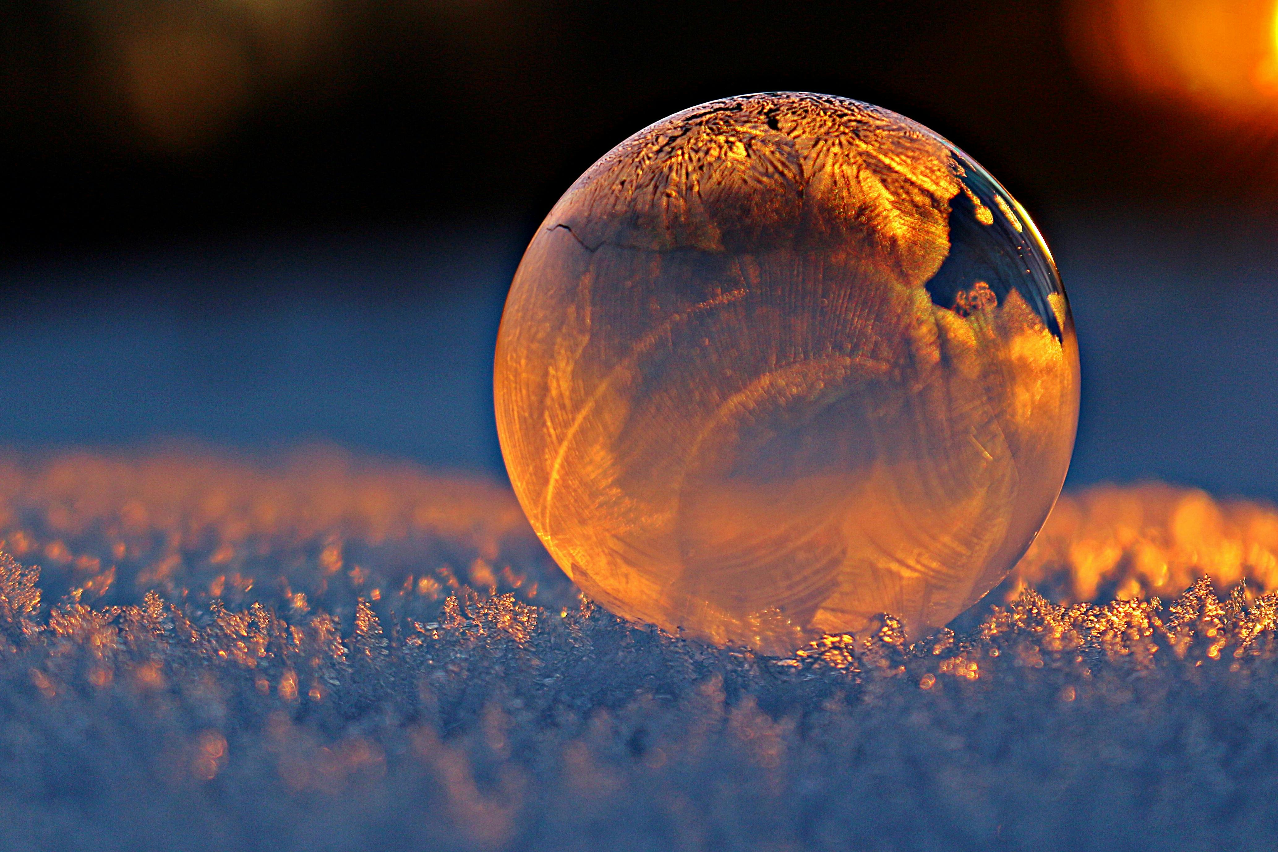 Frozen soap bubble resting on snow in golden sunset light