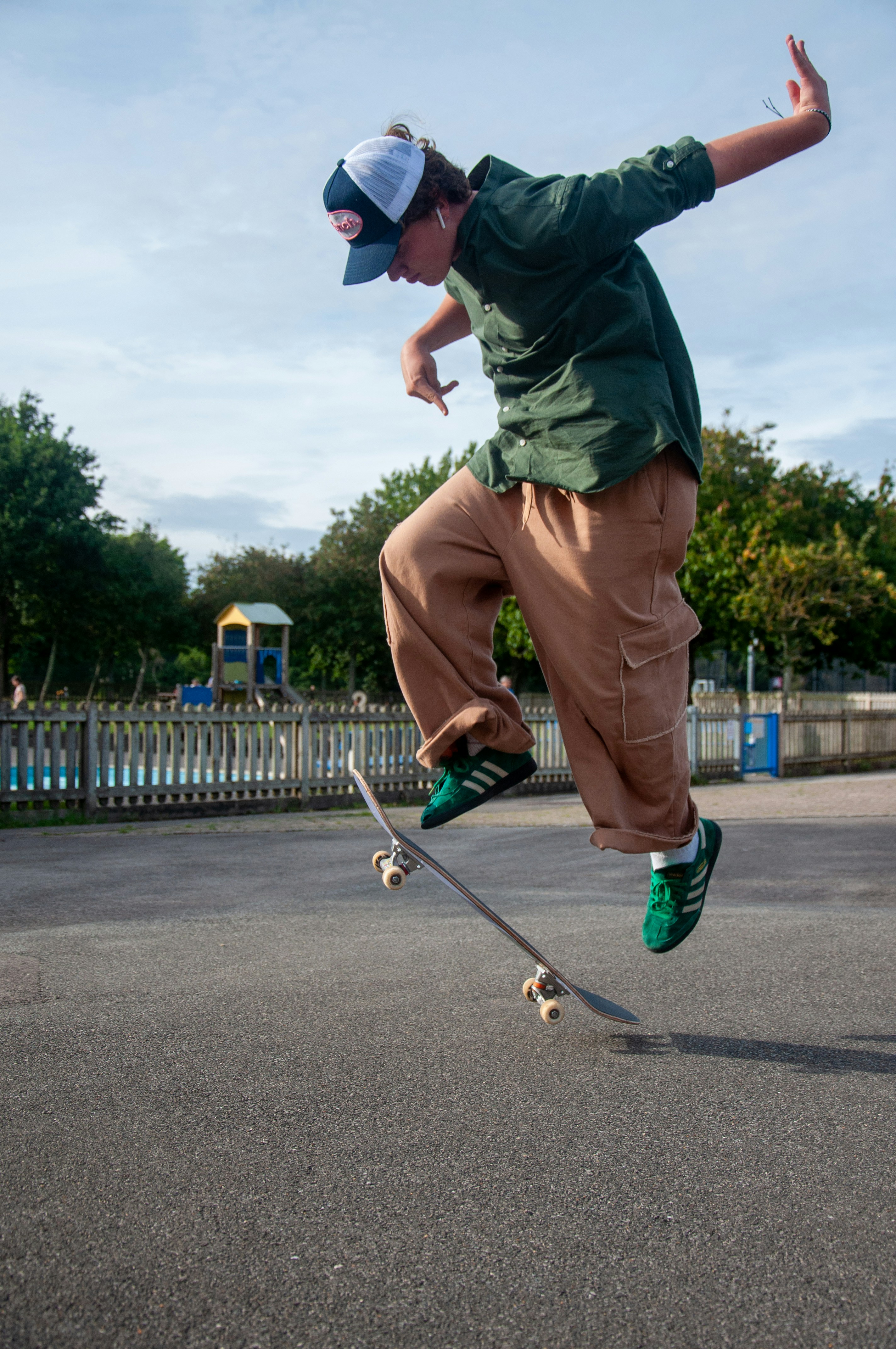 A skateboarder wearing brown cargo pants and green sneakers mid-air while performing a trick at a skatepark.