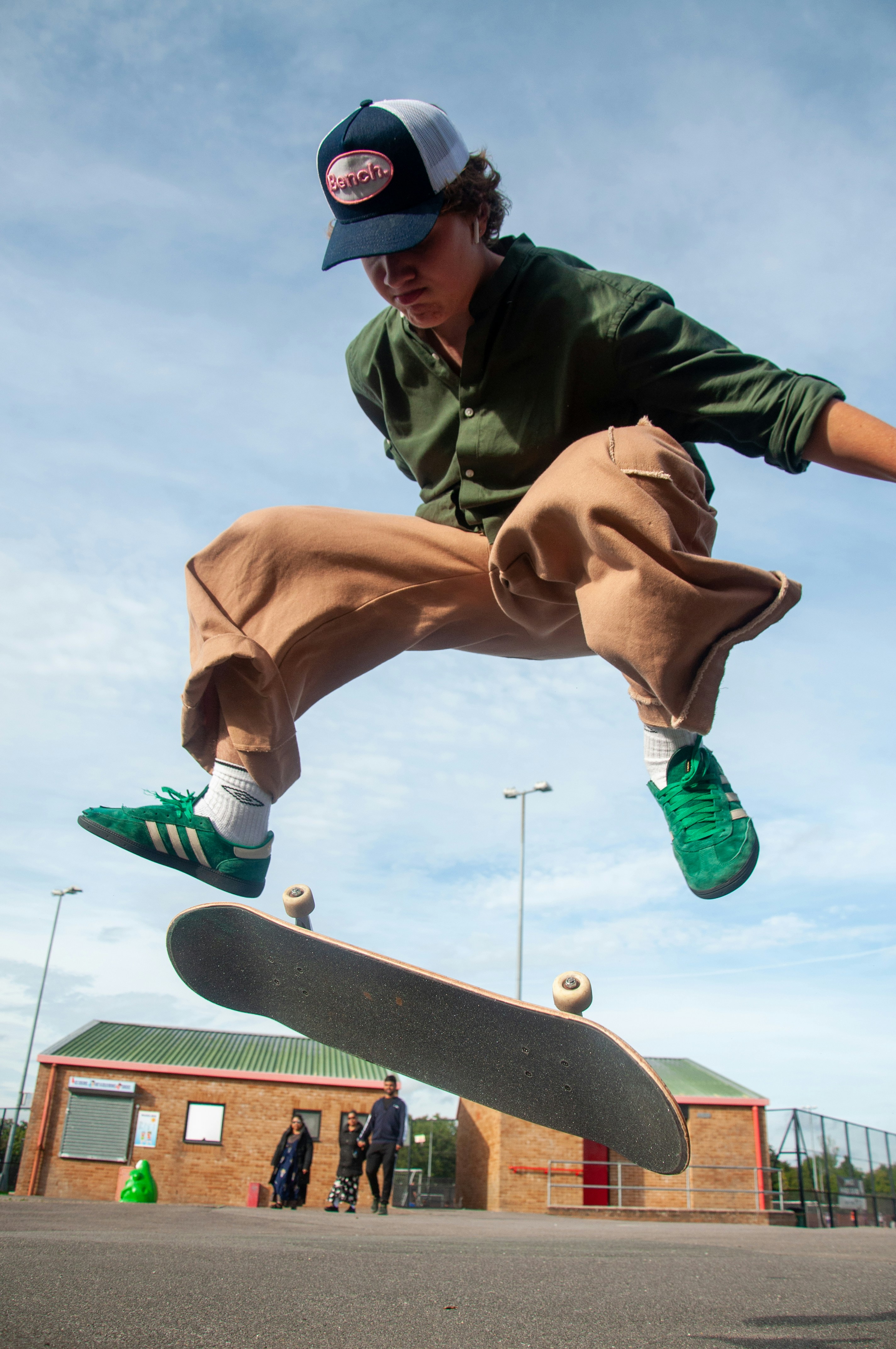 A dynamic, low-angle close-up of a skateboarder's legs and green sneakers as they jump high into the air with their board below them.