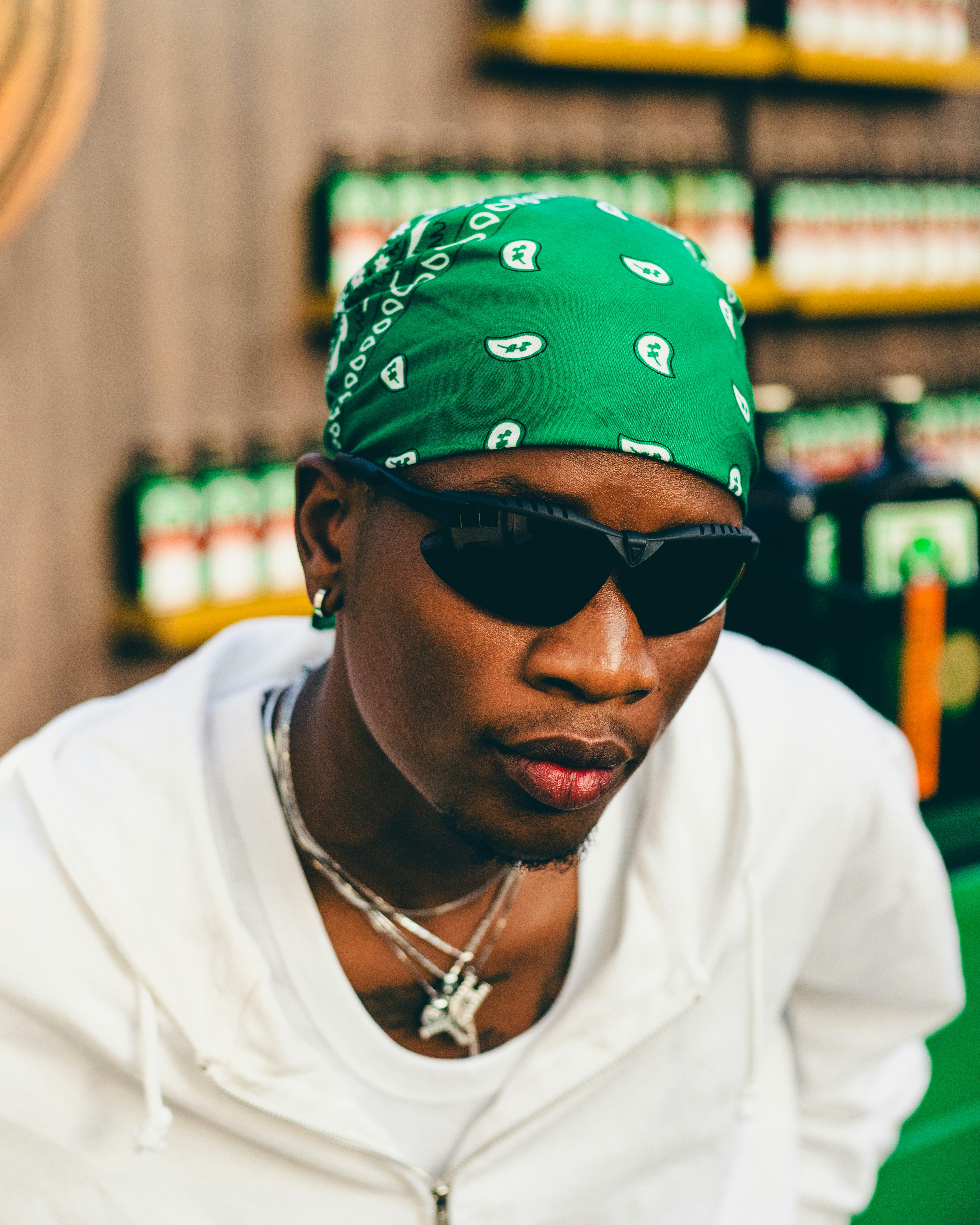 A close-up portrait of the man in the green bandana and sunglasses, looking directly into the camera with a serious expression.