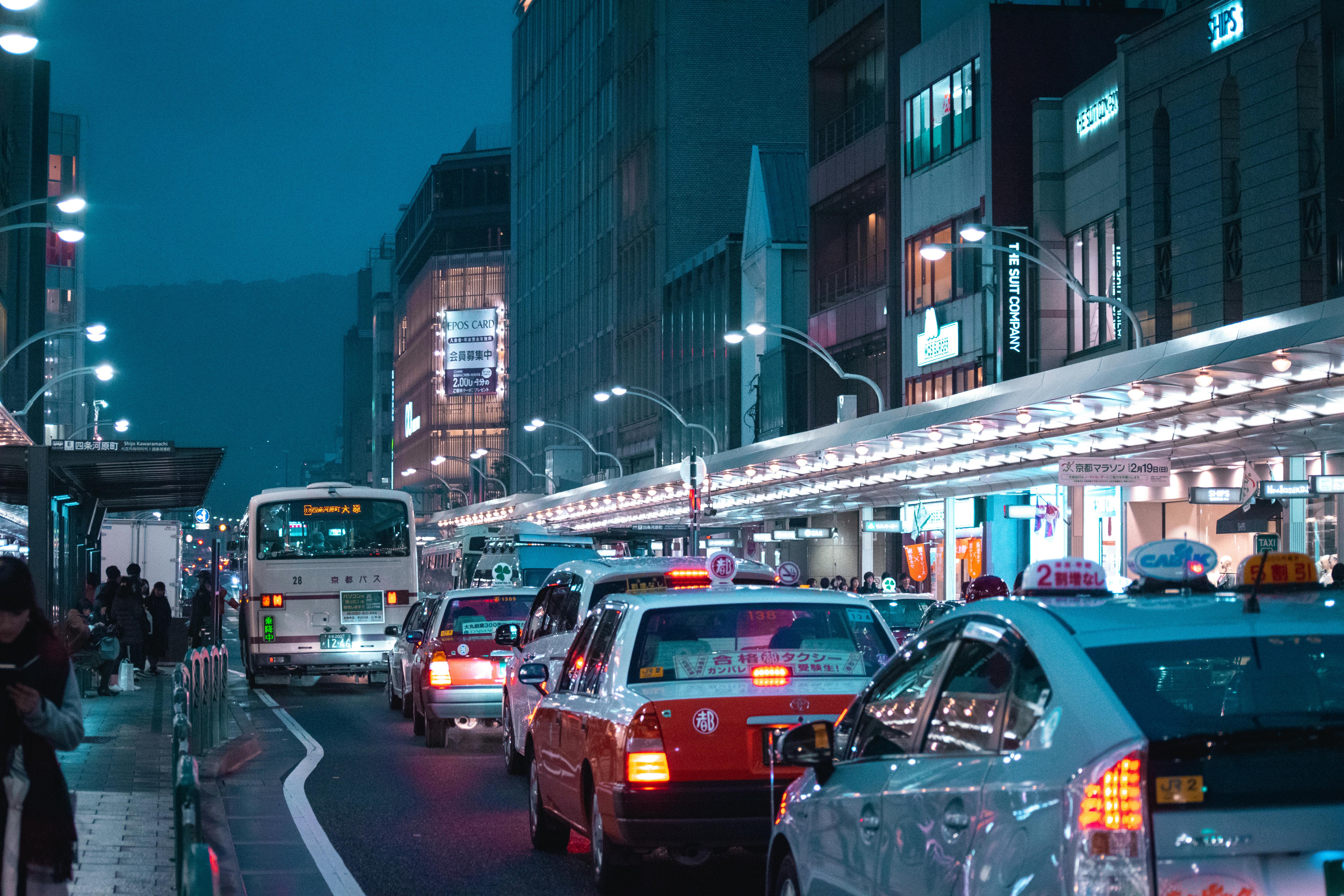 Busy Tokyo street at night, filled with bright neon signs, buses, and colorful taxis in traffic.