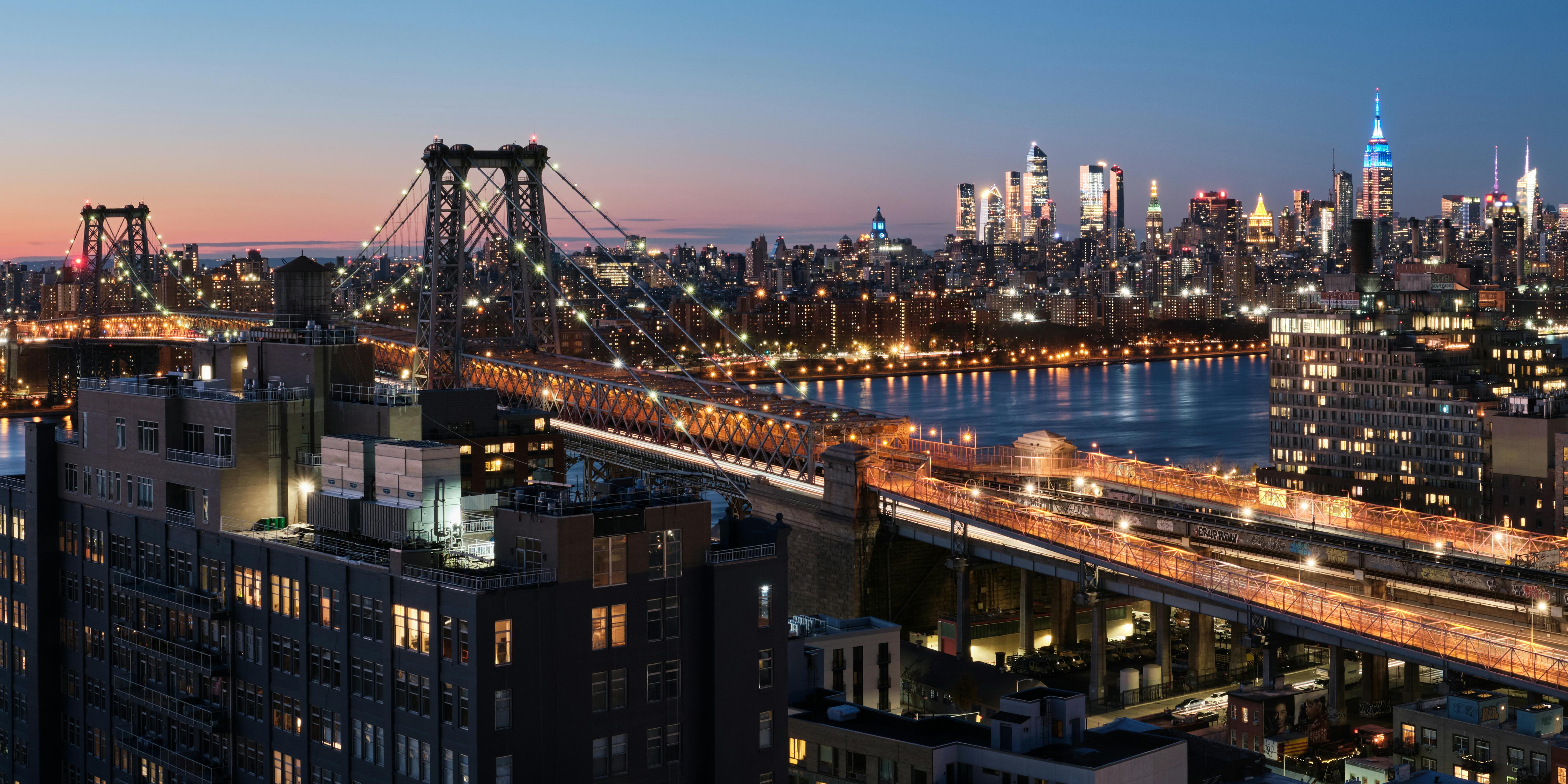 Wide twilight view of the New York City skyline and the Williamsburg Bridge spanning the East River.