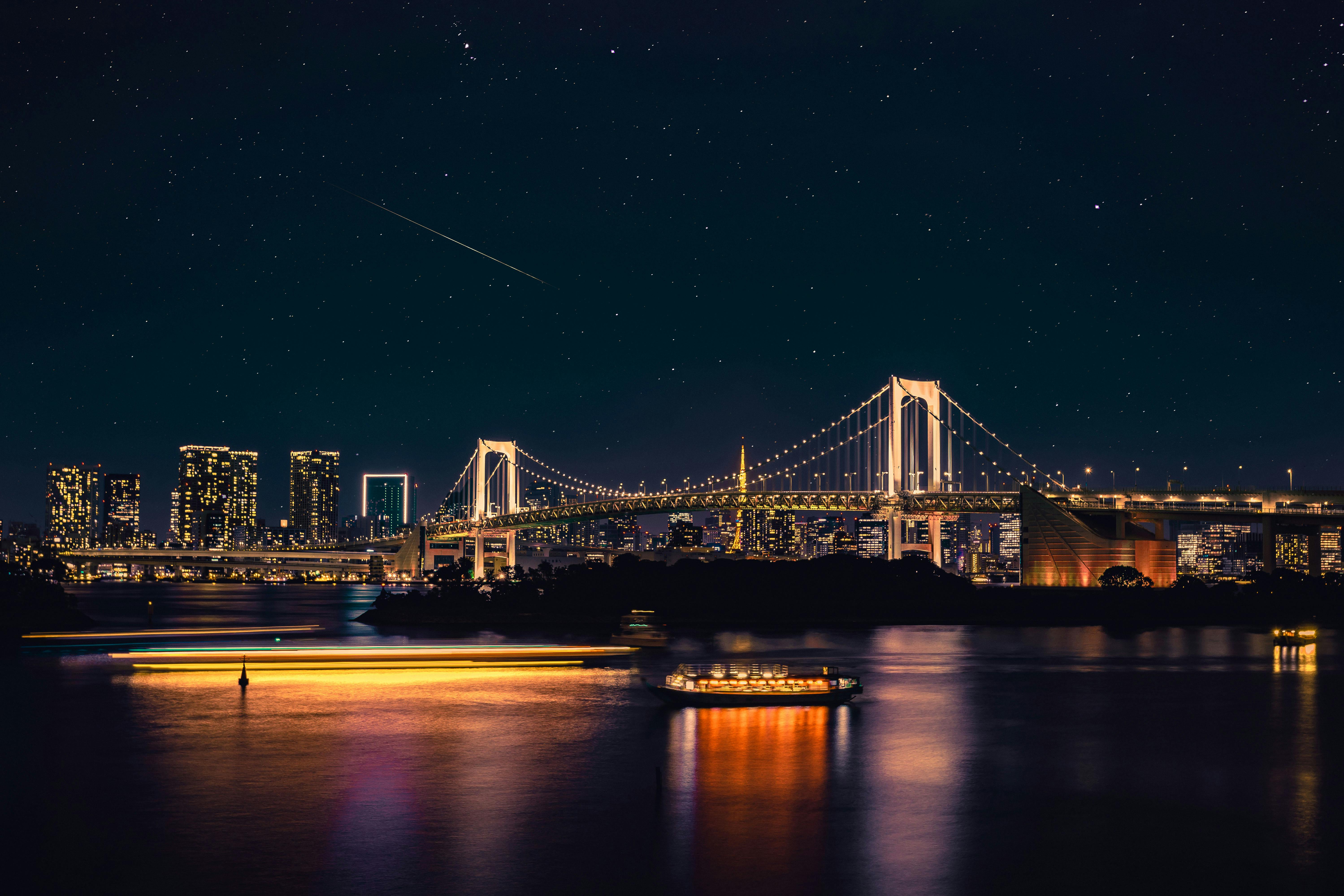Tokyo Rainbow Bridge lit up at night with a cruise boat on the water