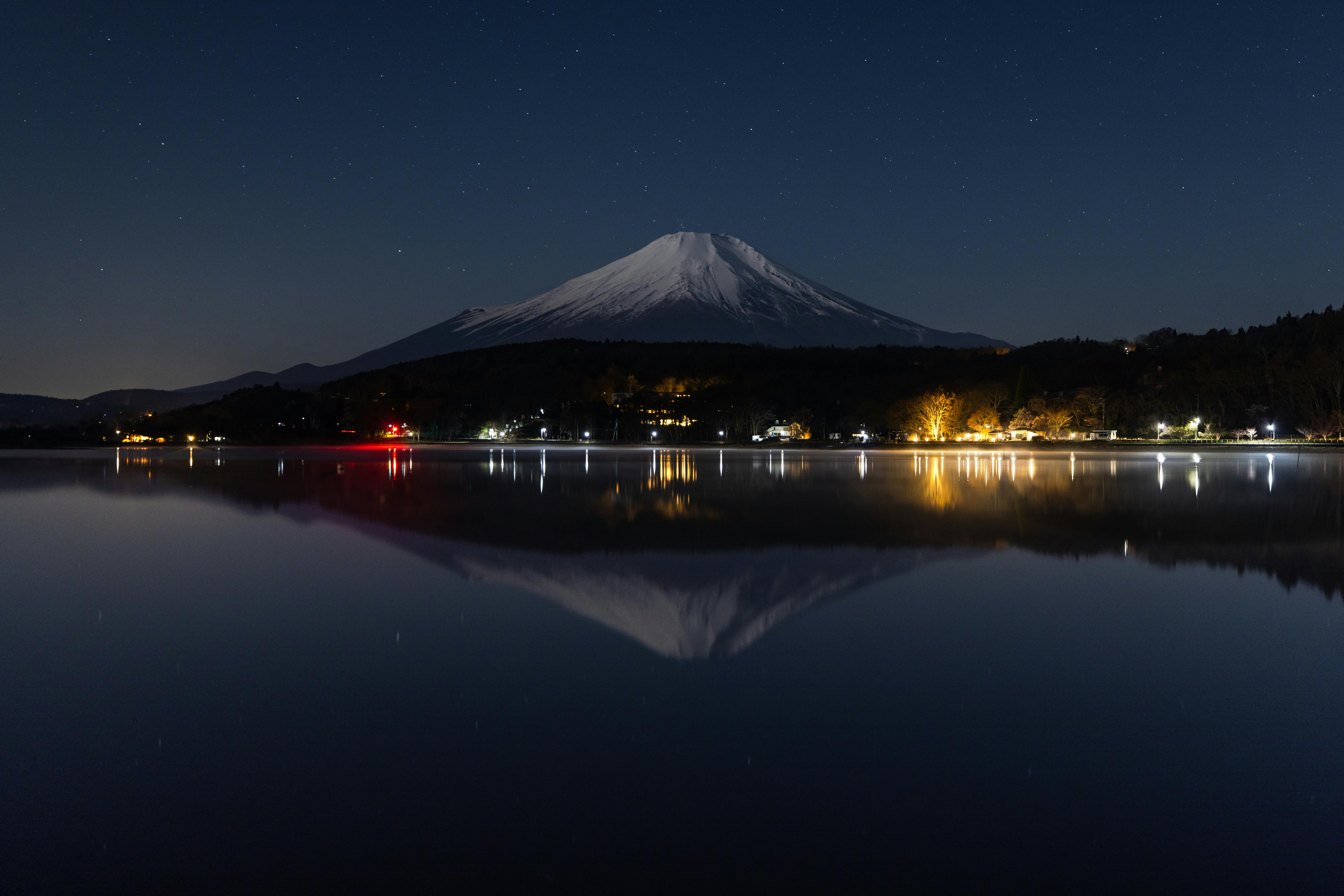 Mount Fuji reflected in a calm dark lake with cherry blossom framing