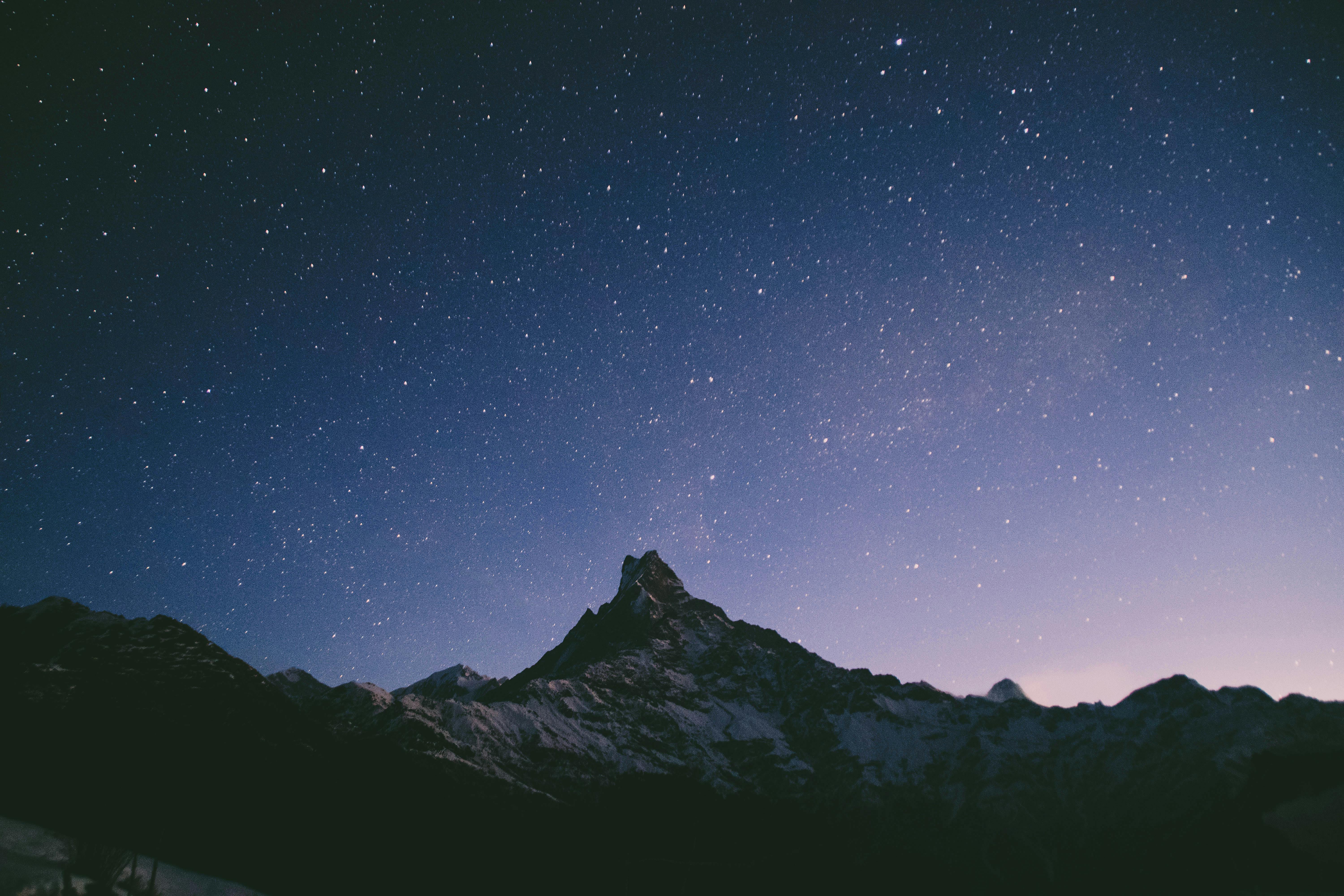 Starry night sky above the silhouette of a jagged mountain peak