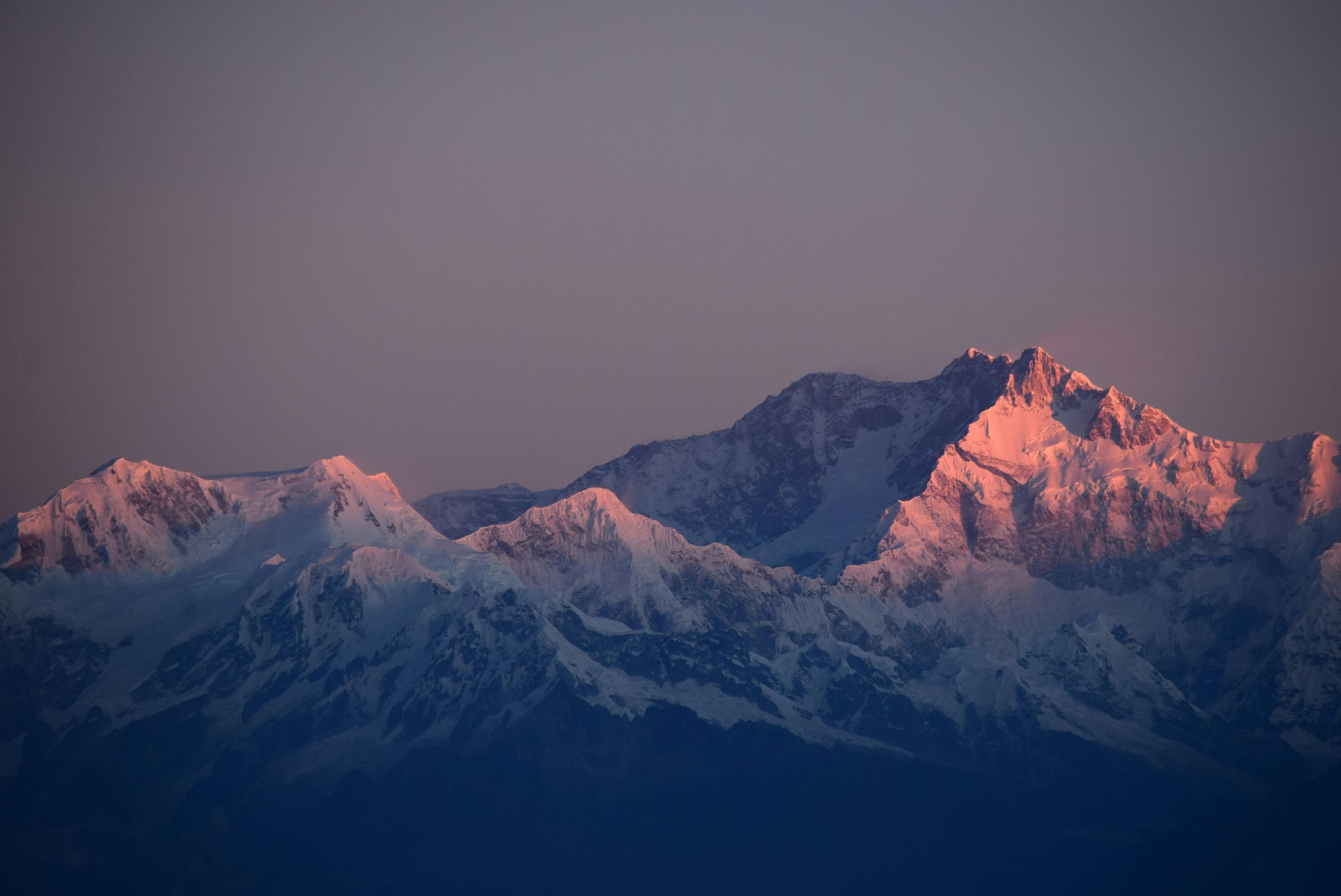 agged, snow-capped mountain peaks bathed in the warm, pinkish-orange light of alpenglow at dawn or dusk.