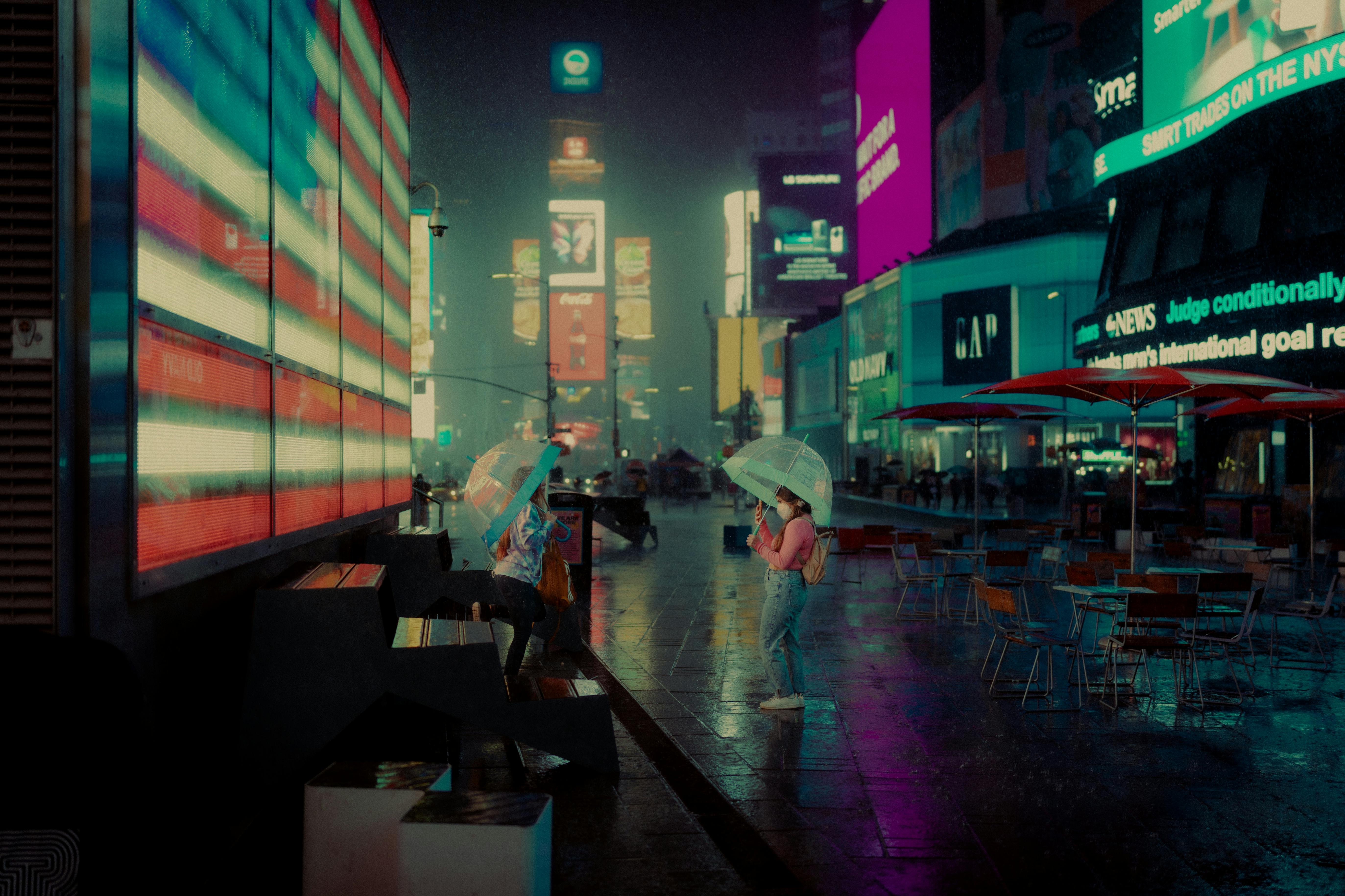 A rainy, vibrant view of Times Square at night with glowing billboards reflecting on the wet ground and a person holding an umbrella.