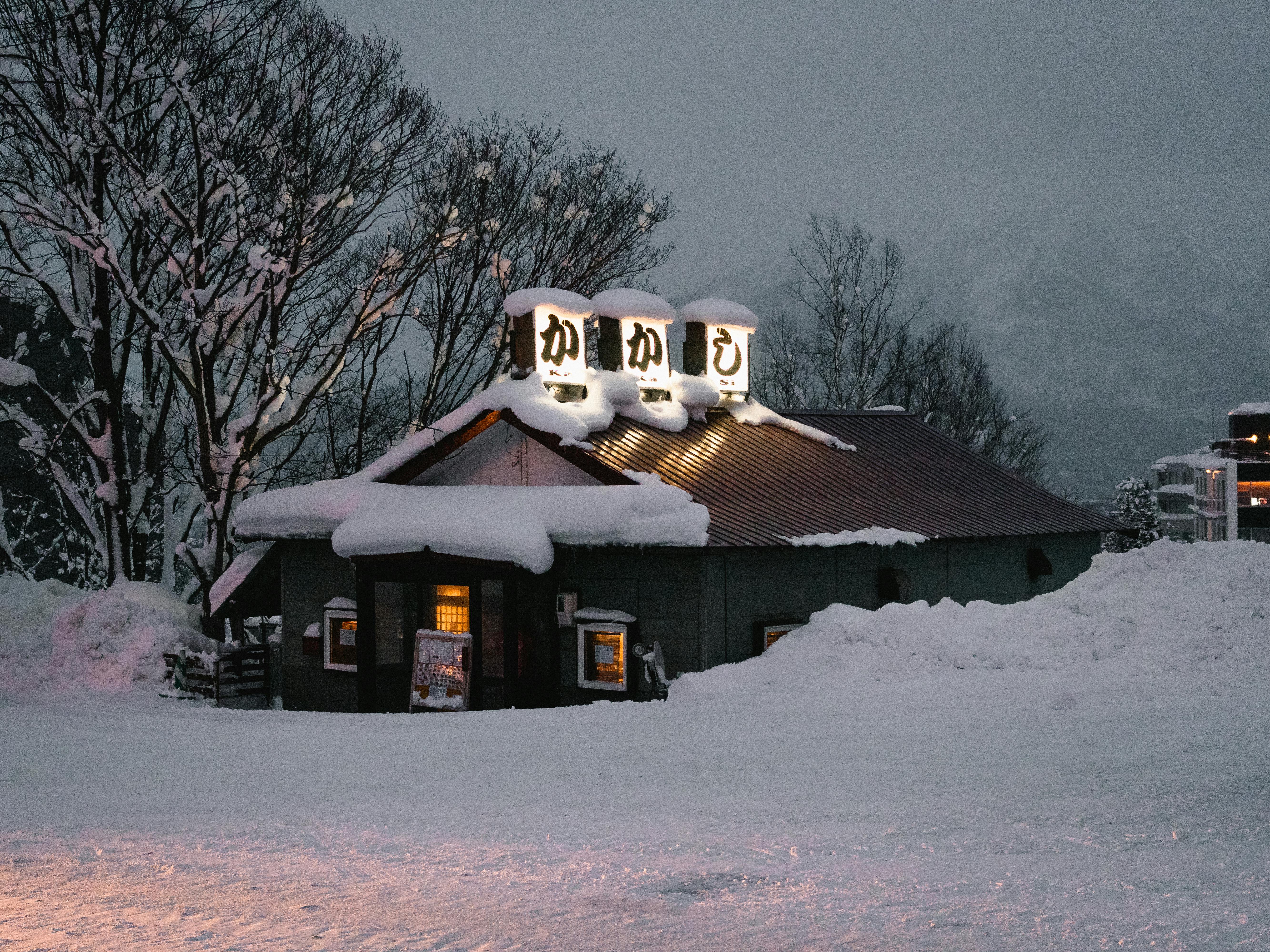 Snow-covered Japanese restaurant glowing warmly at winter dusk