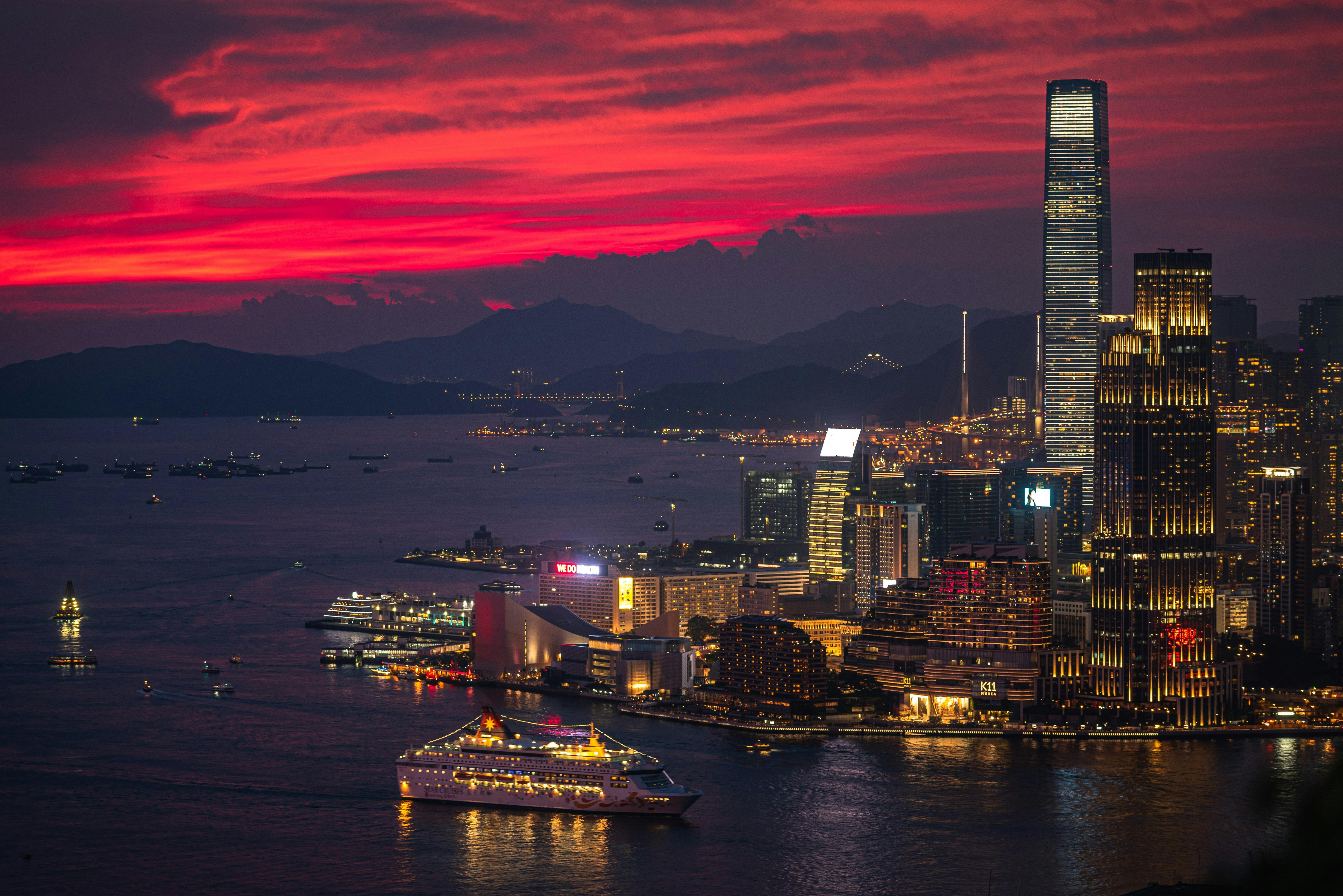 A stunning night view of Victoria Harbour in Hong Kong with a vibrant deep red sunset sky and city lights reflecting on the water.