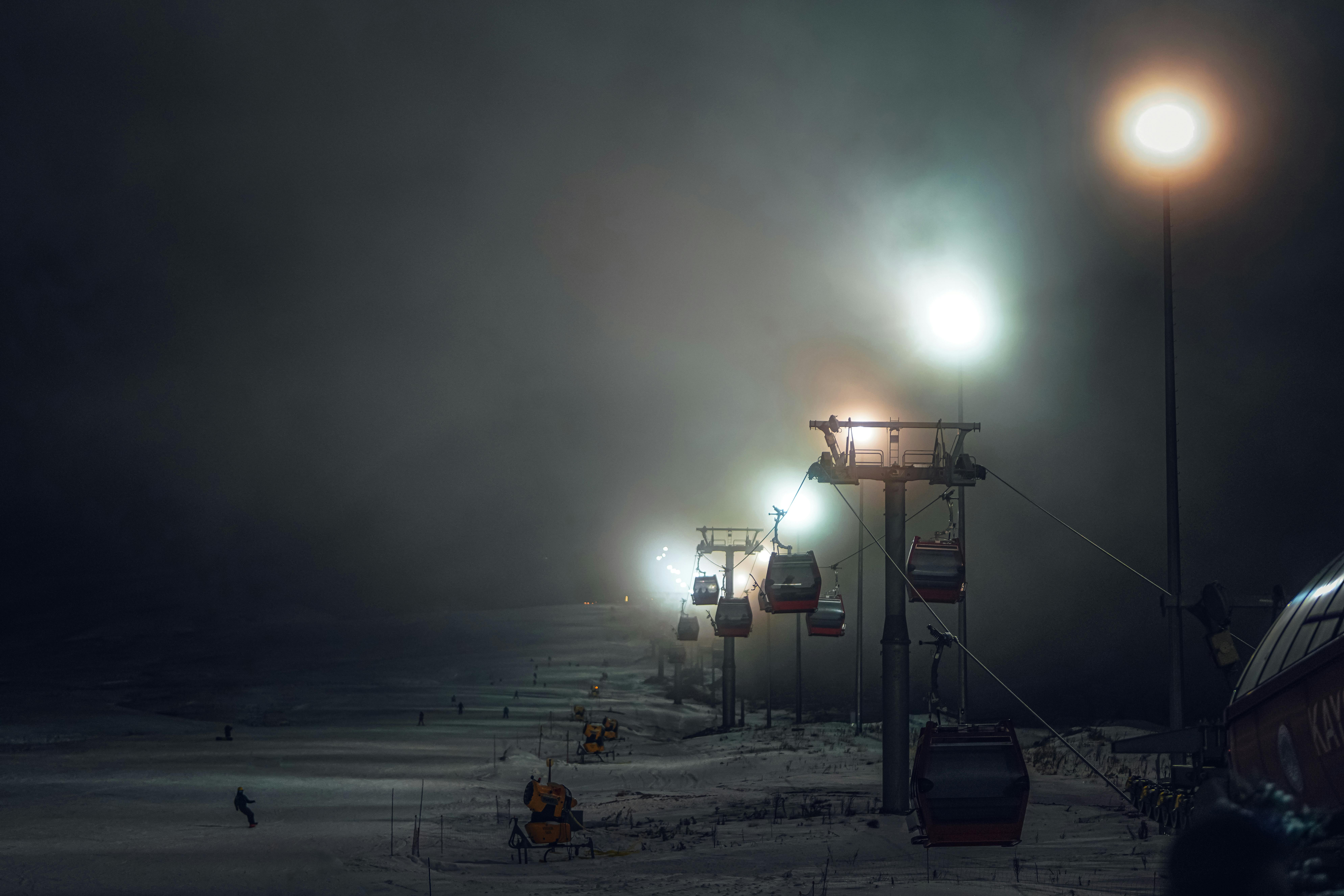 A series of cable cars ascending into a thick, eerie fog at night, illuminated by soft, hazy streetlights.
