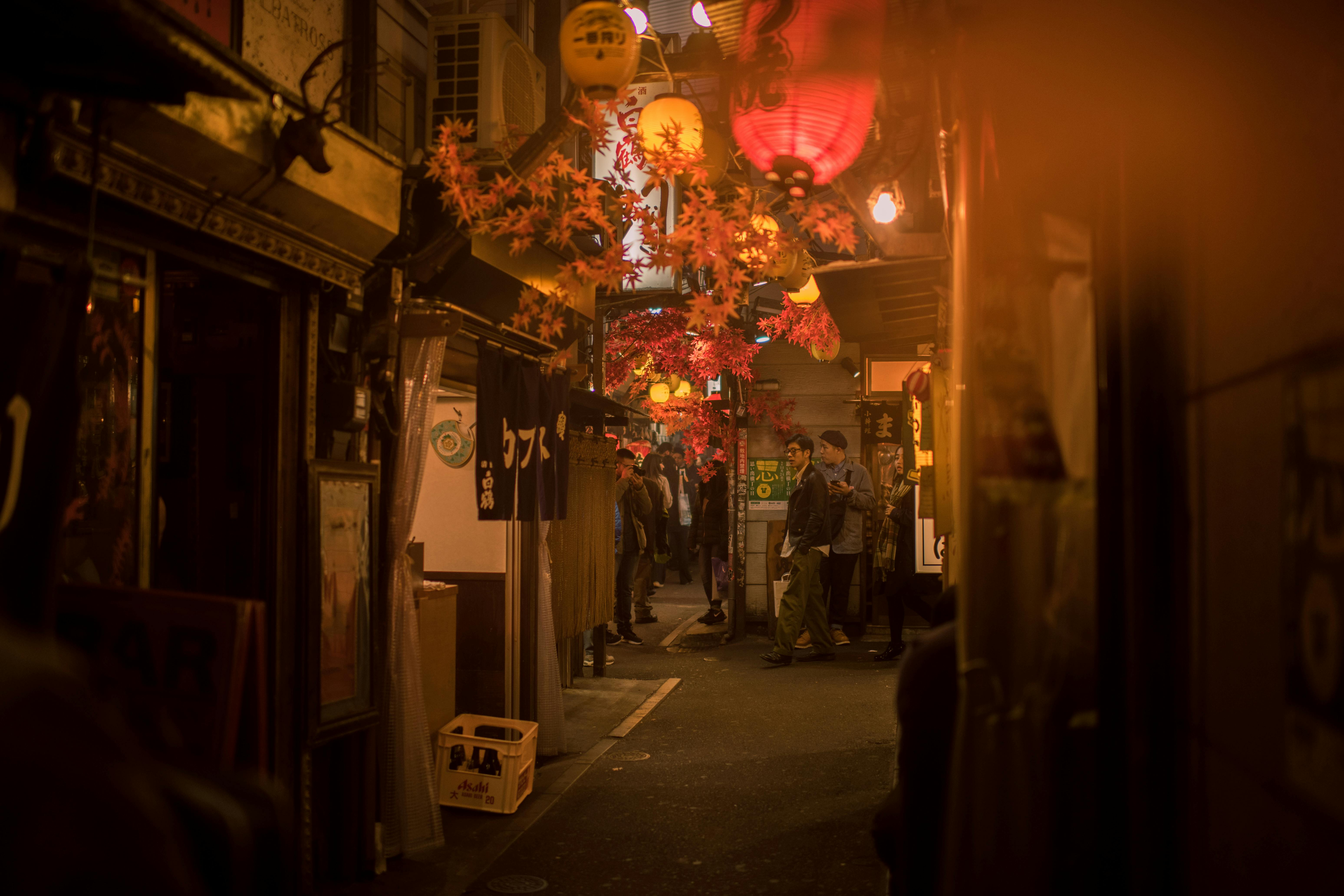 A warm, atmospheric view of an Omoide Yokocho-style alleyway in Tokyo, filled with the glow of lanterns and cozy small restaurants.