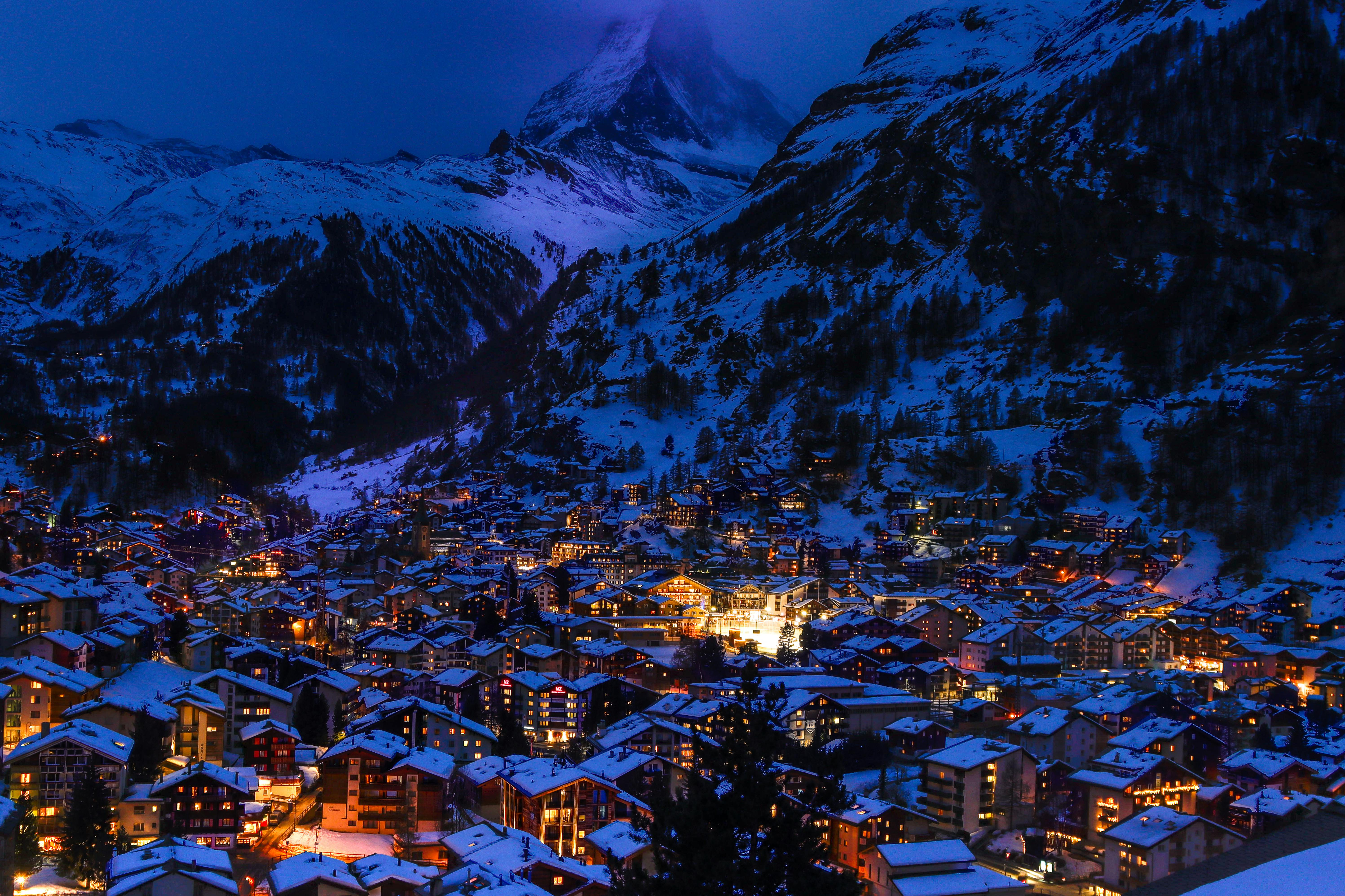 Blue hour aerial view of the snow-covered village of Zermatt, Switzerland, with the towering silhouette of the Matterhorn in the background.